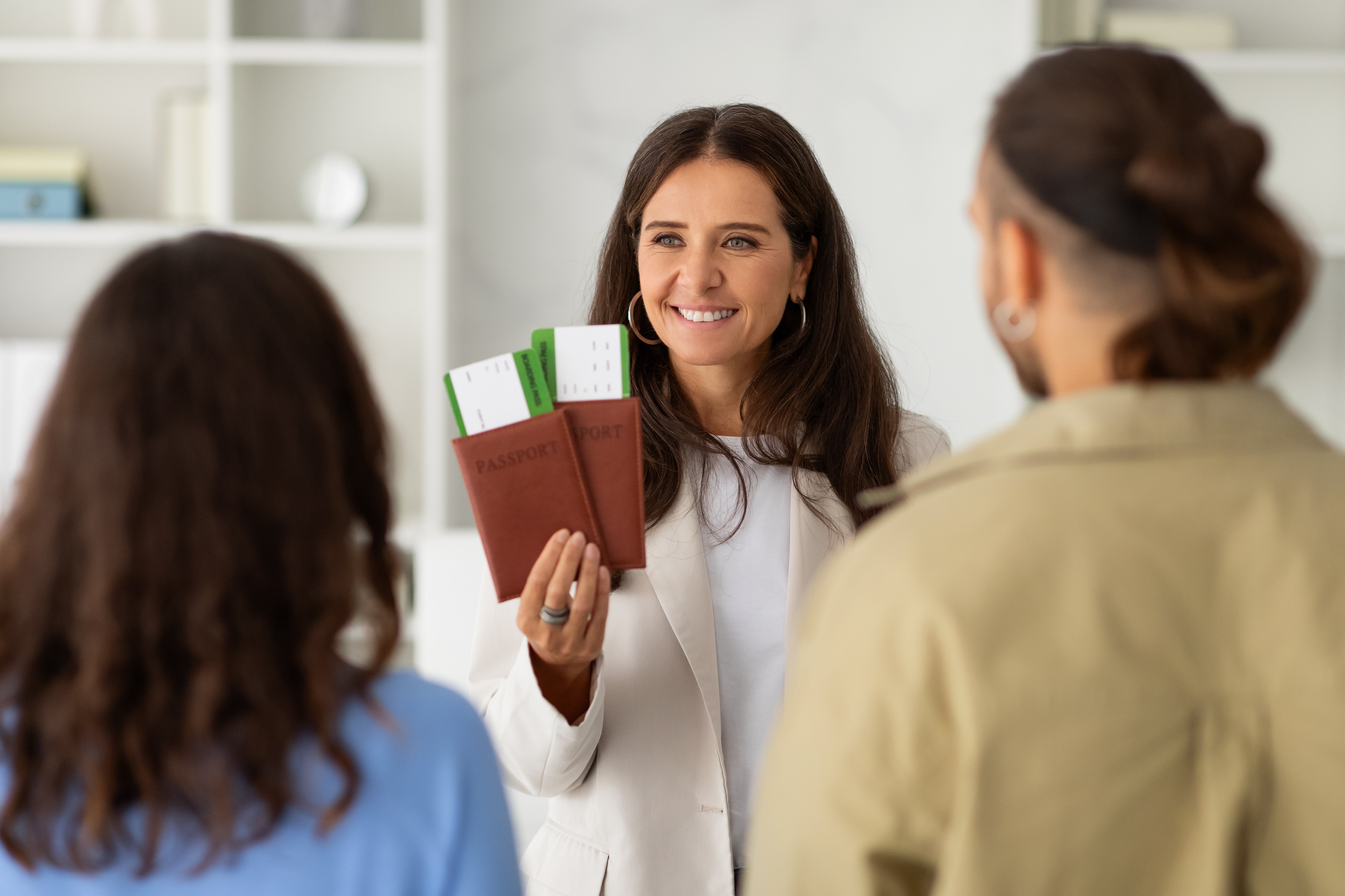 Young couple meeting with a travel agent or visa manager. Mature woman agency worker sitting at her office desk with a man and woman, looking at them and holding their tickets and passports